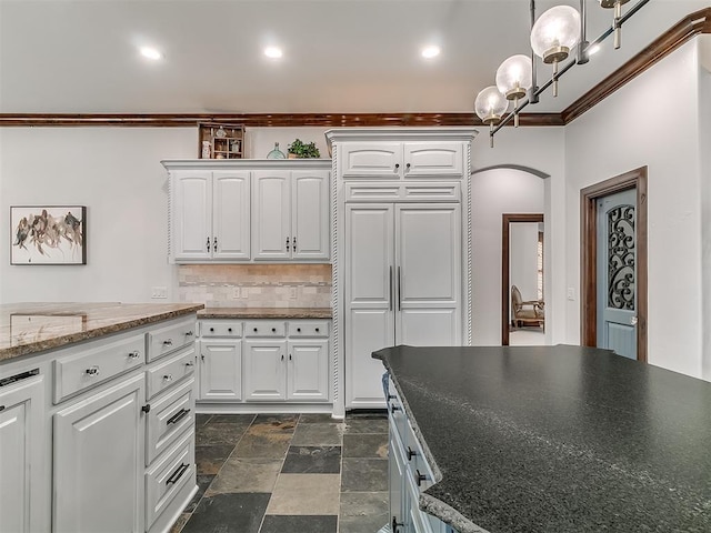 kitchen featuring hanging light fixtures, dark stone counters, decorative backsplash, white cabinets, and ornamental molding