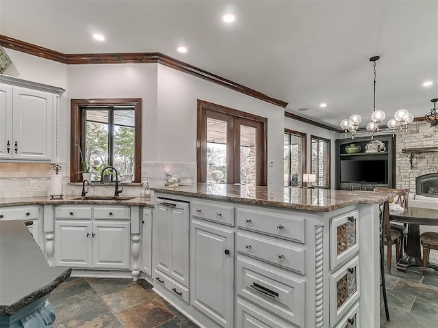 kitchen featuring decorative backsplash, white cabinetry, a stone fireplace, and sink