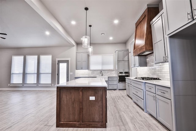 kitchen featuring a center island, hanging light fixtures, appliances with stainless steel finishes, tasteful backsplash, and light hardwood / wood-style floors