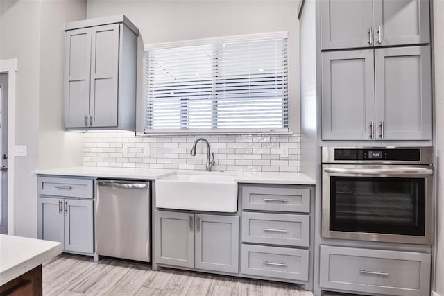 kitchen featuring backsplash, sink, gray cabinets, light hardwood / wood-style floors, and stainless steel appliances