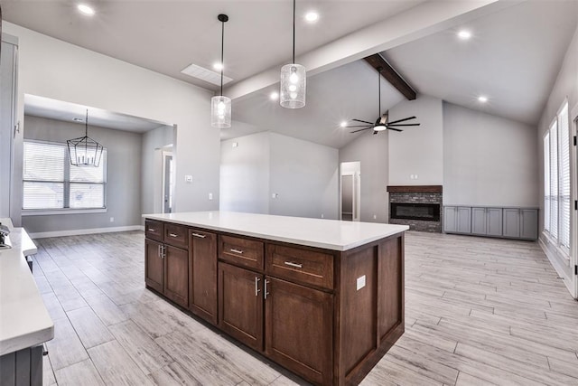 kitchen with lofted ceiling with beams, light hardwood / wood-style floors, a kitchen island, hanging light fixtures, and a stone fireplace