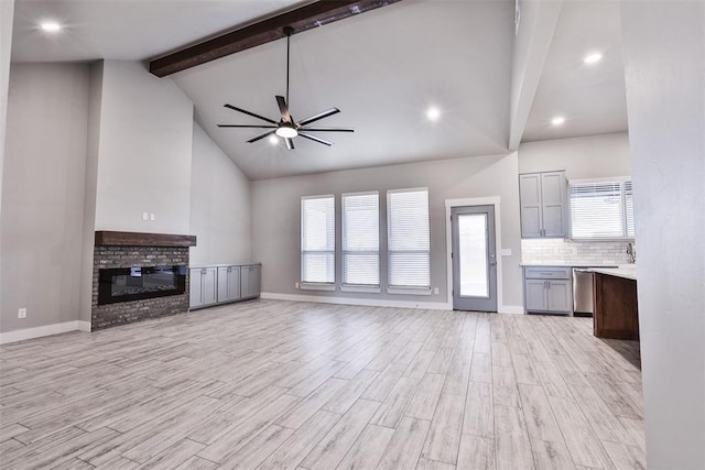 unfurnished living room with high vaulted ceiling, a brick fireplace, light hardwood / wood-style flooring, ceiling fan, and beamed ceiling