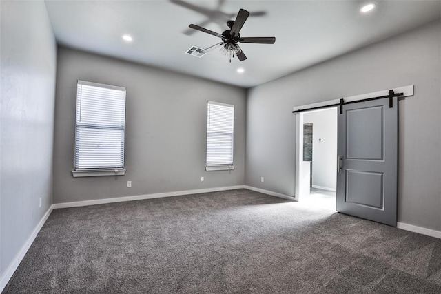 unfurnished bedroom with dark colored carpet, a barn door, multiple windows, and ceiling fan