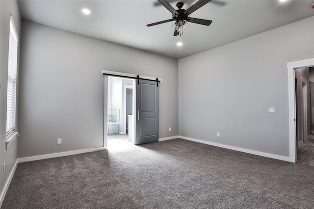 unfurnished bedroom with dark colored carpet, a barn door, and ceiling fan