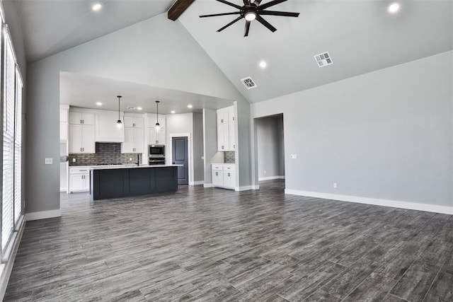 unfurnished living room featuring dark hardwood / wood-style floors, beam ceiling, plenty of natural light, and ceiling fan