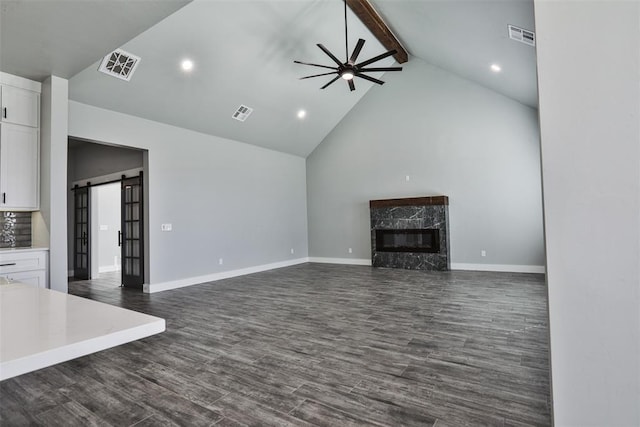 unfurnished living room featuring a high end fireplace, ceiling fan, dark wood-type flooring, beam ceiling, and a barn door