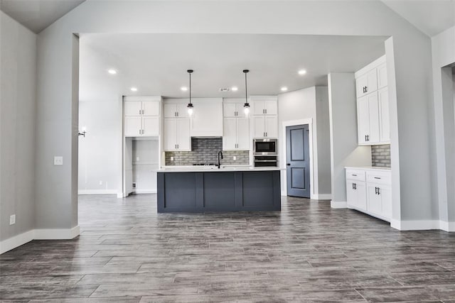 kitchen featuring hanging light fixtures, an island with sink, white cabinetry, wood-type flooring, and stainless steel appliances