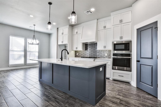 kitchen featuring stainless steel appliances, white cabinetry, premium range hood, and an island with sink