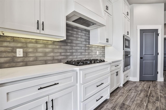 kitchen featuring appliances with stainless steel finishes, premium range hood, tasteful backsplash, dark wood-type flooring, and white cabinets