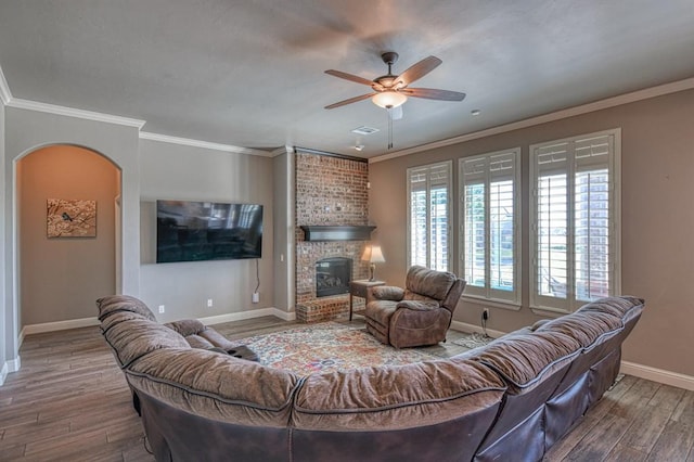 living room with ceiling fan, hardwood / wood-style floors, ornamental molding, and a brick fireplace