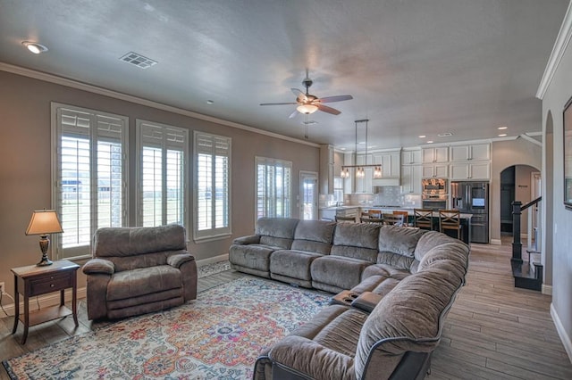 31814 Landrun Ave, Norman, OK 73072 - living room featuring arched walkways, ceiling fan, light wood finished floors, healthy amount of natural light, and ornamental molding
