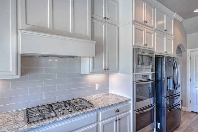 kitchen with light stone countertops, wood-type flooring, decorative backsplash, white cabinets, and appliances with stainless steel finishes