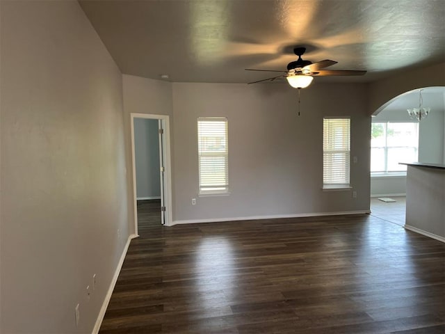 empty room with ceiling fan with notable chandelier, plenty of natural light, and dark wood-type flooring