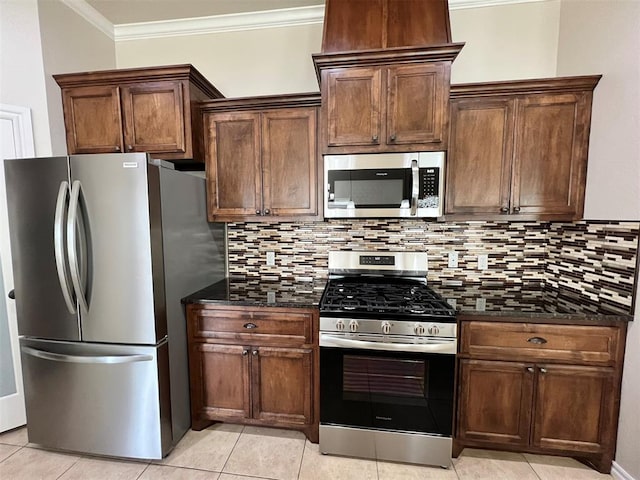 kitchen with stainless steel appliances, tasteful backsplash, dark stone counters, light tile patterned flooring, and ornamental molding