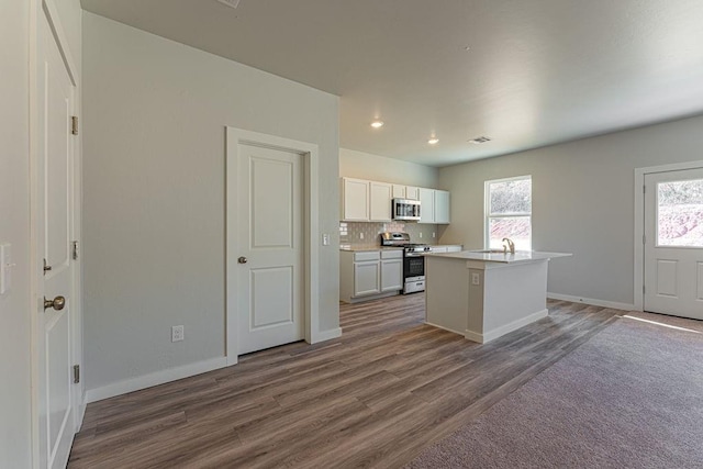 kitchen with a wealth of natural light, white cabinets, stainless steel appliances, and a kitchen island with sink