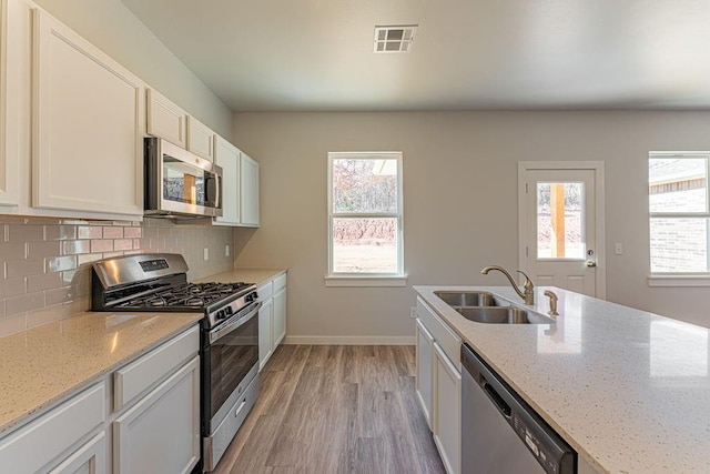 kitchen featuring light stone countertops, white cabinetry, decorative backsplash, sink, and stainless steel appliances