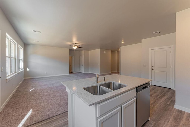 kitchen featuring light stone countertops, stainless steel dishwasher, sink, white cabinets, and an island with sink