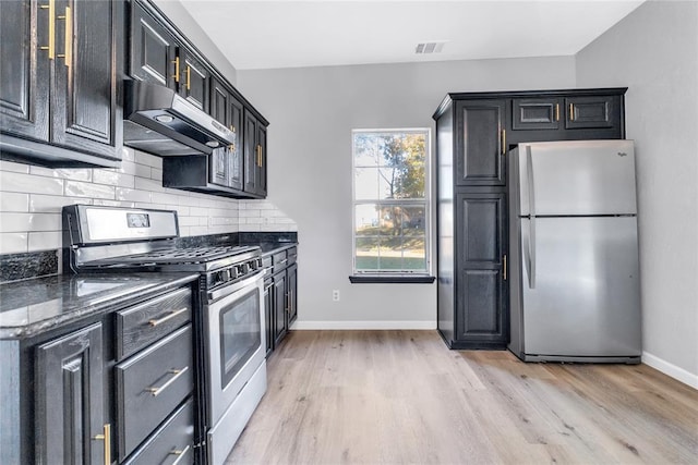 kitchen with light hardwood / wood-style floors, dark stone countertops, stainless steel appliances, and tasteful backsplash