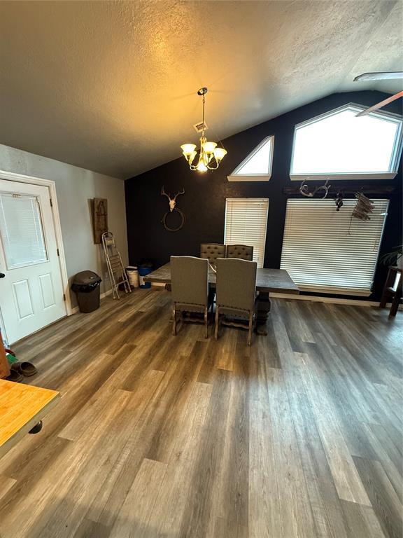 dining area with hardwood / wood-style floors, lofted ceiling, a textured ceiling, and an inviting chandelier