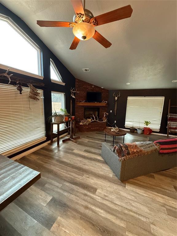 living room featuring a brick fireplace, light hardwood / wood-style flooring, ceiling fan, and lofted ceiling