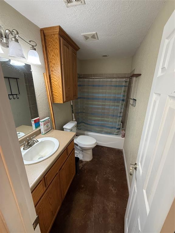 full bathroom featuring shower / bath combo with shower curtain, vanity, a textured ceiling, and toilet