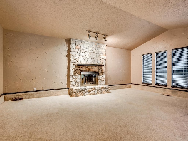 unfurnished living room with carpet flooring, a textured ceiling, a stone fireplace, and vaulted ceiling