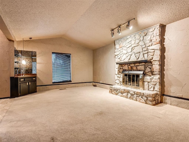 unfurnished living room featuring carpet flooring, a textured ceiling, sink, a stone fireplace, and lofted ceiling