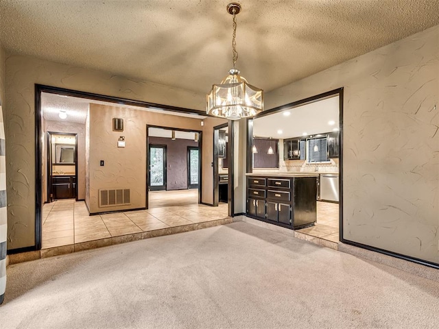 interior space with stainless steel dishwasher, light colored carpet, hanging light fixtures, and a textured ceiling