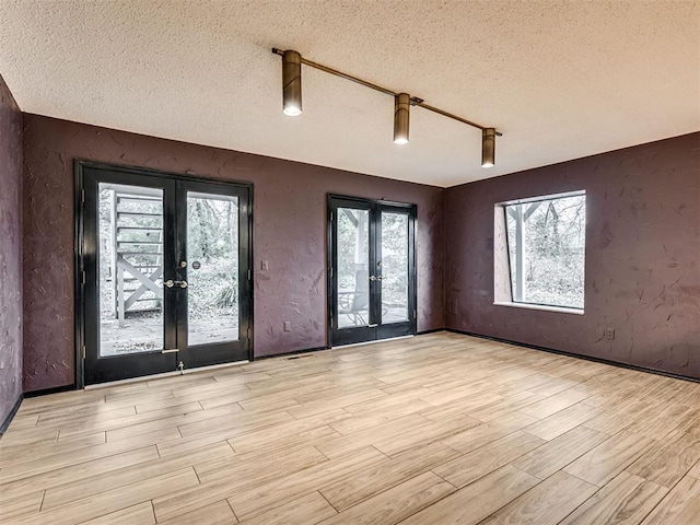 empty room with a healthy amount of sunlight, french doors, light hardwood / wood-style floors, and a textured ceiling