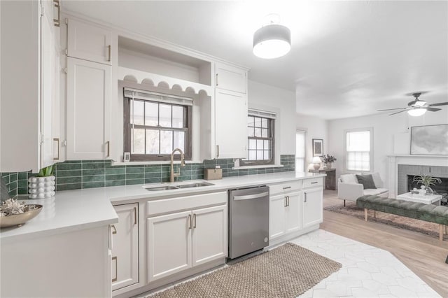 kitchen featuring sink, ceiling fan, dishwasher, white cabinets, and a brick fireplace