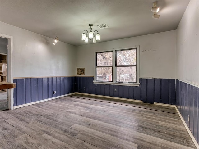 unfurnished room with a chandelier, wood-type flooring, and wood walls