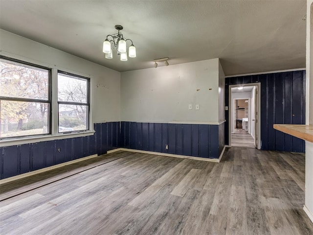 spare room with a chandelier, wood-type flooring, and wood walls