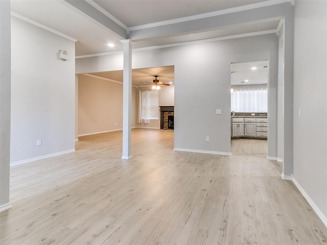 empty room featuring crown molding, a fireplace, ceiling fan, and light wood-type flooring