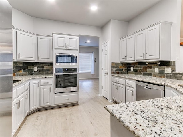 kitchen with light stone countertops, white cabinetry, stainless steel appliances, and light hardwood / wood-style flooring