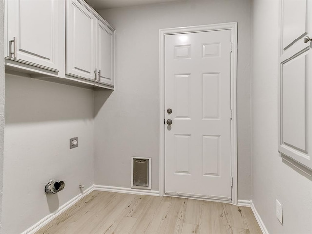 laundry area with electric dryer hookup, light hardwood / wood-style floors, and cabinets