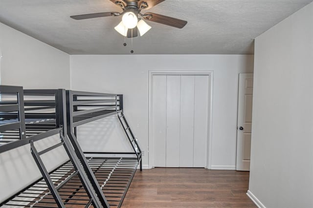 bedroom with a textured ceiling, ceiling fan, dark wood-type flooring, and a closet