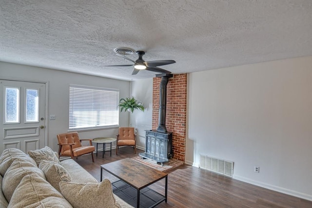 living room featuring a textured ceiling, dark hardwood / wood-style floors, a wood stove, and ceiling fan