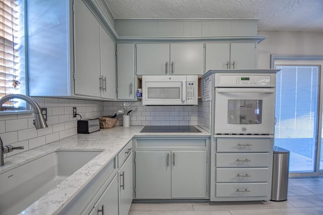 kitchen with white appliances, sink, a textured ceiling, light tile patterned flooring, and light stone counters