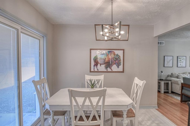 dining room with a textured ceiling, light hardwood / wood-style flooring, and a notable chandelier