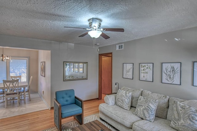 living room featuring ceiling fan with notable chandelier, a textured ceiling, and light hardwood / wood-style flooring