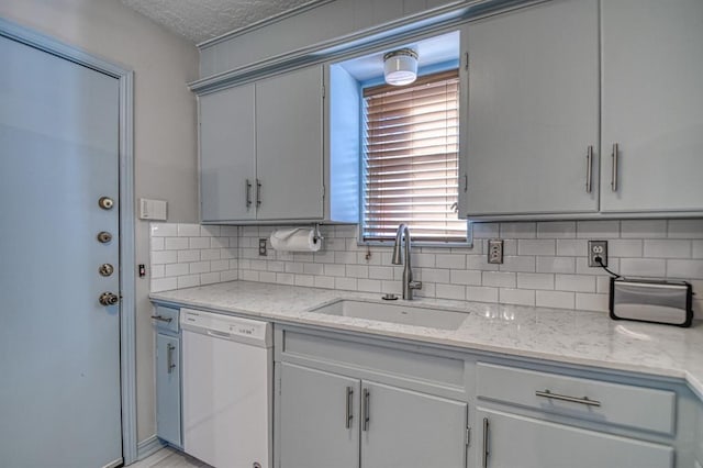 kitchen featuring dishwasher, tasteful backsplash, light stone counters, and sink