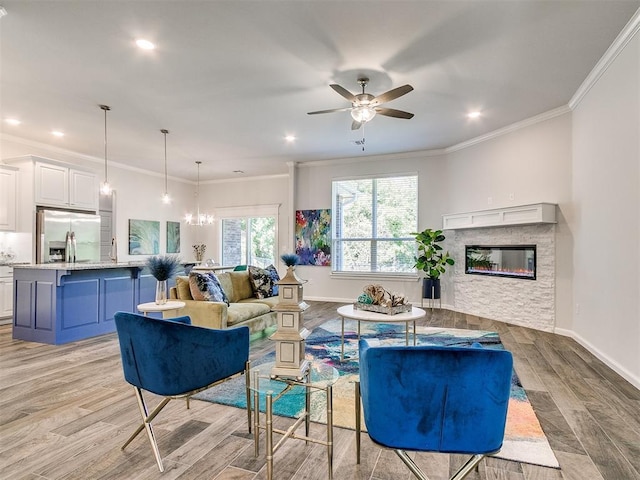 living room featuring ceiling fan, ornamental molding, a fireplace, and light hardwood / wood-style flooring