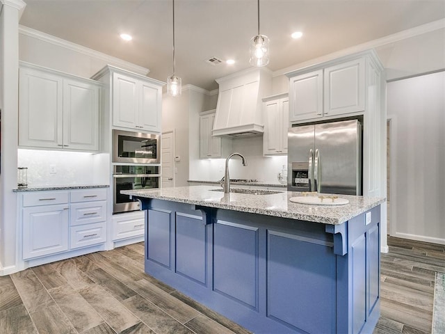 kitchen featuring stainless steel appliances, an island with sink, decorative light fixtures, white cabinets, and light wood-type flooring