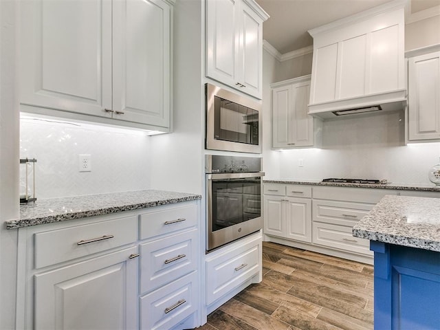 kitchen featuring light stone countertops, white cabinetry, crown molding, hardwood / wood-style floors, and appliances with stainless steel finishes