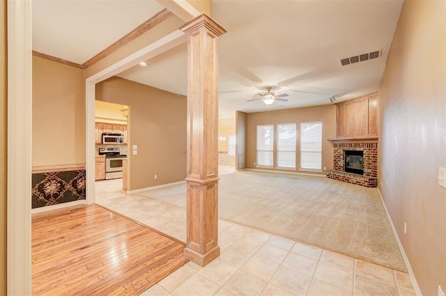 unfurnished living room featuring ceiling fan, a brick fireplace, decorative columns, crown molding, and light wood-type flooring