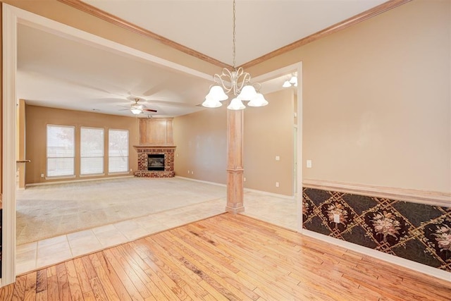 unfurnished living room featuring hardwood / wood-style floors, ceiling fan with notable chandelier, ornamental molding, and a brick fireplace