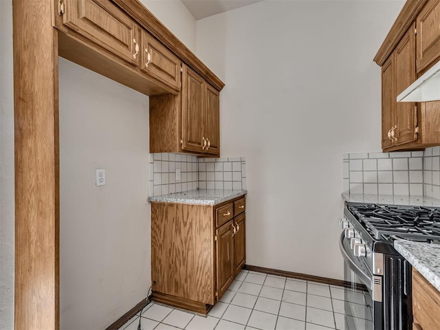 kitchen with wall chimney exhaust hood, light tile patterned floors, tasteful backsplash, gas stove, and light stone counters