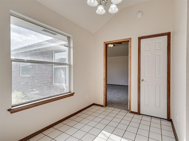 tiled empty room with plenty of natural light, an inviting chandelier, and vaulted ceiling