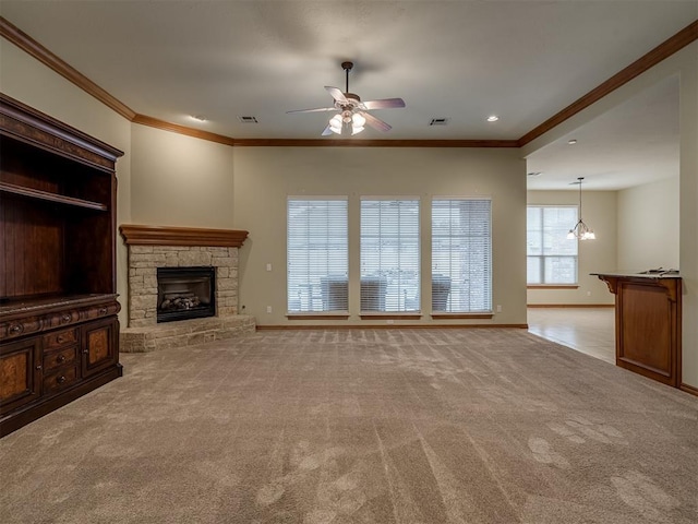 unfurnished living room with light carpet, ceiling fan with notable chandelier, a stone fireplace, and crown molding