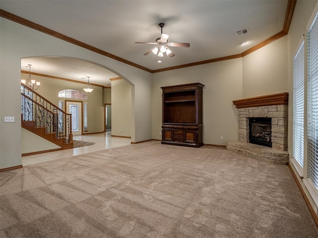 unfurnished living room featuring ceiling fan with notable chandelier, light colored carpet, a stone fireplace, and crown molding